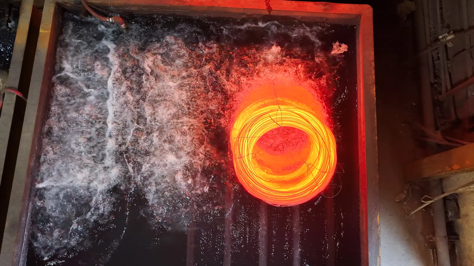 A red-hot coil of wire glowing in a quench bath during heat treating
